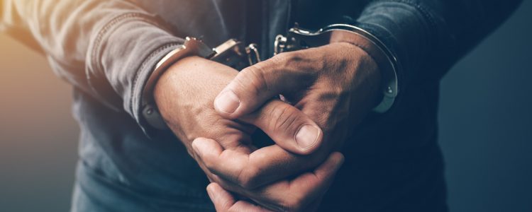 Arrested computer hacker and cyber criminal with handcuffs, close up of hands