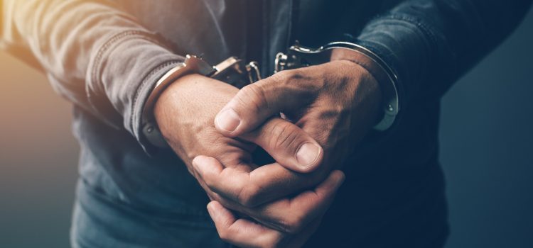 Arrested computer hacker and cyber criminal with handcuffs, close up of hands